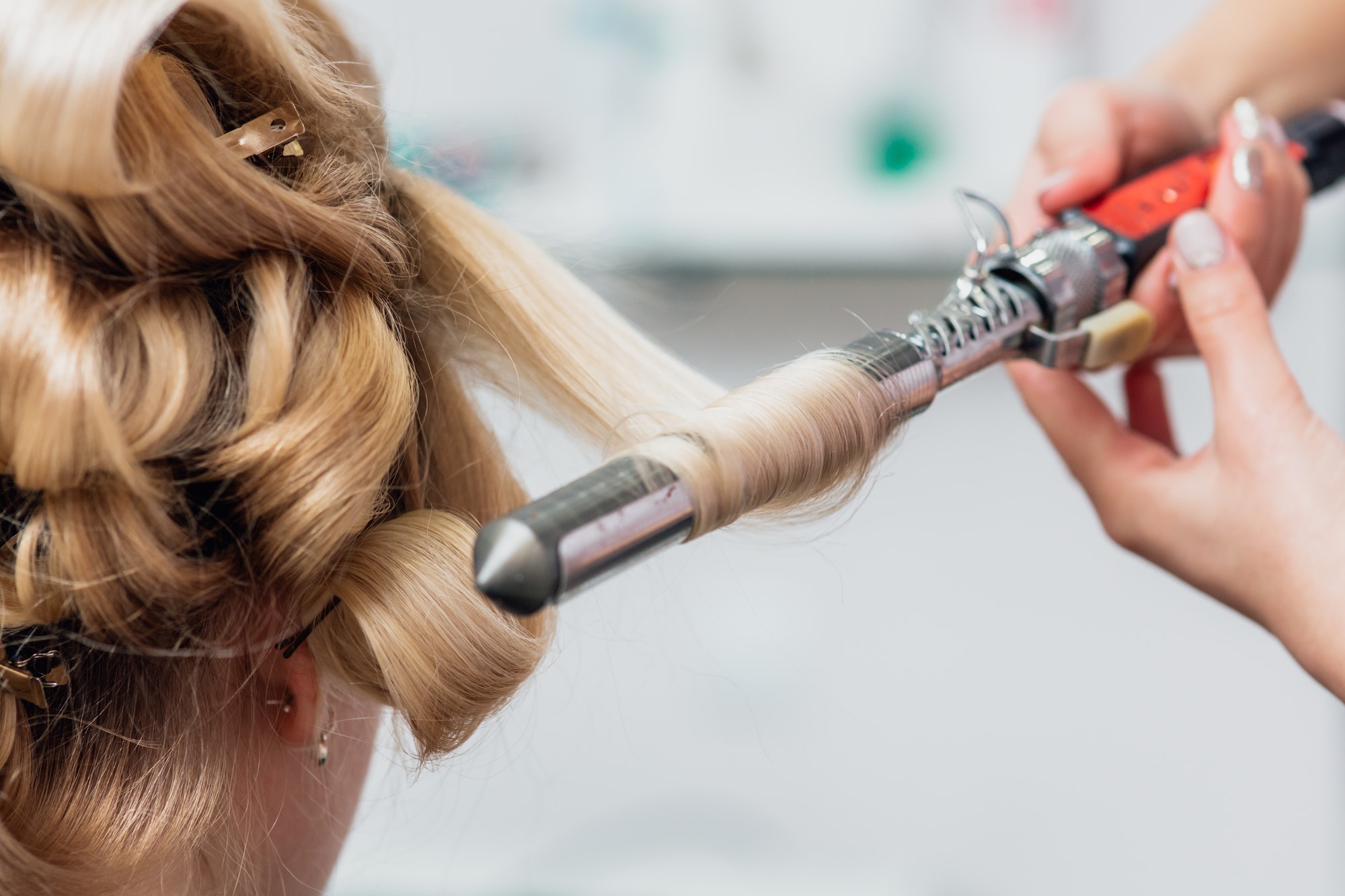 Straightening and curling of blonde hair in hairstyle salon with iron